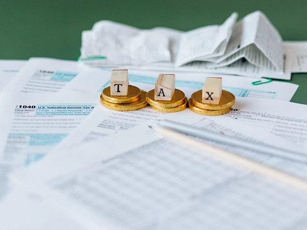 Goldene Münzen mit dem Aufdruck "TAX" liegen auf einer Ansammlung von Steuerformularen, Quittungen und einem Bleistift.