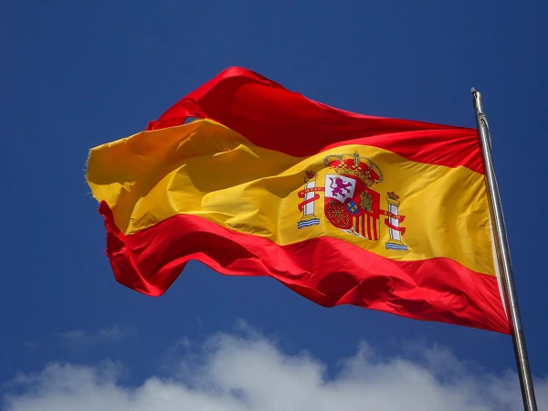 Die Flagge Spaniens weht im Wind vor einem blauen Himmel mit einigen weißen Wolken.