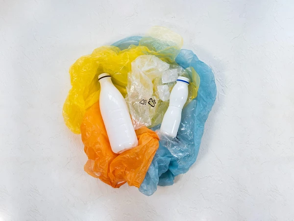 Zwei weiße Plastikflaschen liegen auf einem bunten Haufen aus verbrauchtem Plastikmüll in Gelb, Orange und Blau.