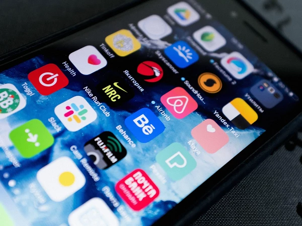 Ein Smartphone-Bildschirm zeigt eine Vielzahl von Apps, darunter Icons für Gesundheit, Nike Club, Airbnb und andere, auf einem blau-grünen Hintergrund.