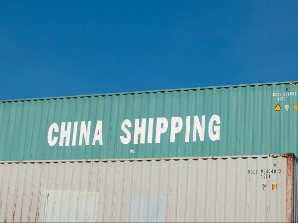 Der obere Teil eines Containerschiffs zeigt einen grünen Frachtcontainer mit der Aufschrift "CHINA SHIPPING" in großen, weißen Buchstaben vor einem klaren, blauen Himmel.