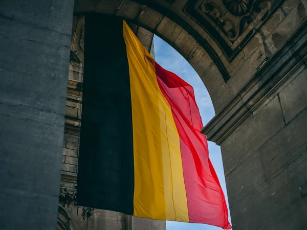 Eine große belgische Flagge hängt zwischen zwei Steinsäulen eines historischer Gebäudes und weht sanft im Wind.