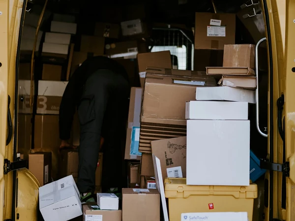 Ein Lieferwagen mit gelber Lackierung ist vollgepackt mit zahlreichen Paketen und Kartons in verschiedenen Größen. Eine Person beugt sich hinein, um ein Paket herauszunehmen.