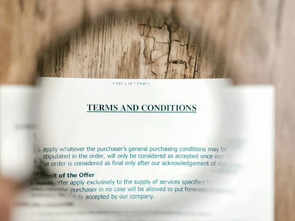 Ein Dokument mit dem Titel „Terms and Conditions“ wird durch eine Lupe vergrößert, während der Hintergrund und die Textdetails verschwommen sind.