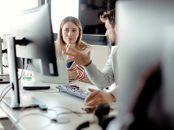 Mitarbeitende im Gespräch vor Monitoren im modernen Büro