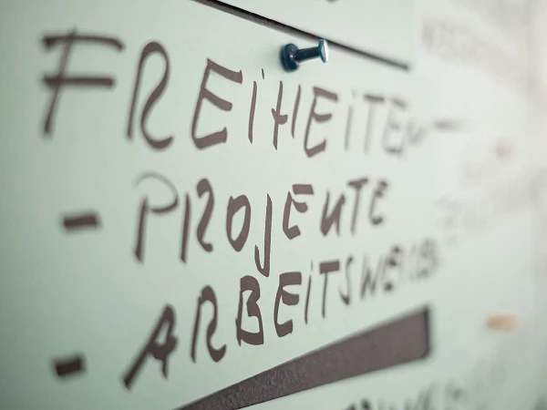 Wand mit handgeschriebenen Wörtern „Freiheiten, Projekte, Arbeitsweise“ – agile Arbeitskultur