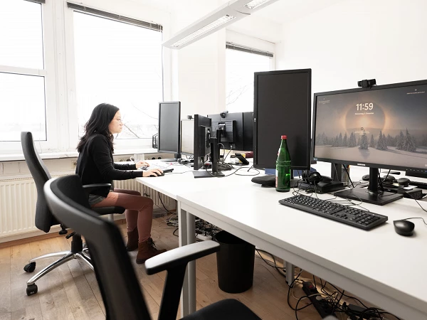 Mitarbeiterin arbeitet konzentriert an mehreren Monitoren im Büro